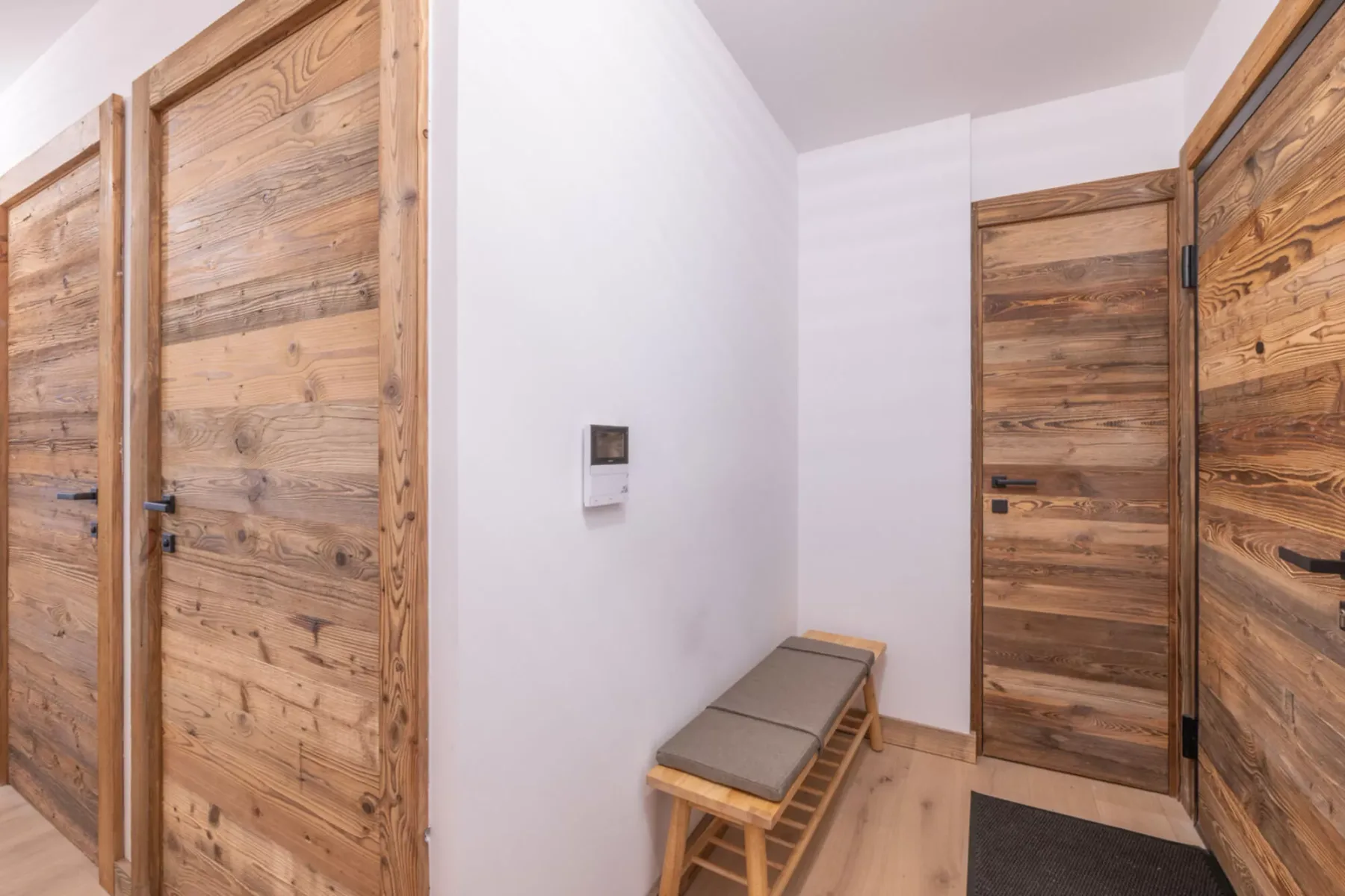 A narrow hallway with wooden doors and a small bench along the wall.