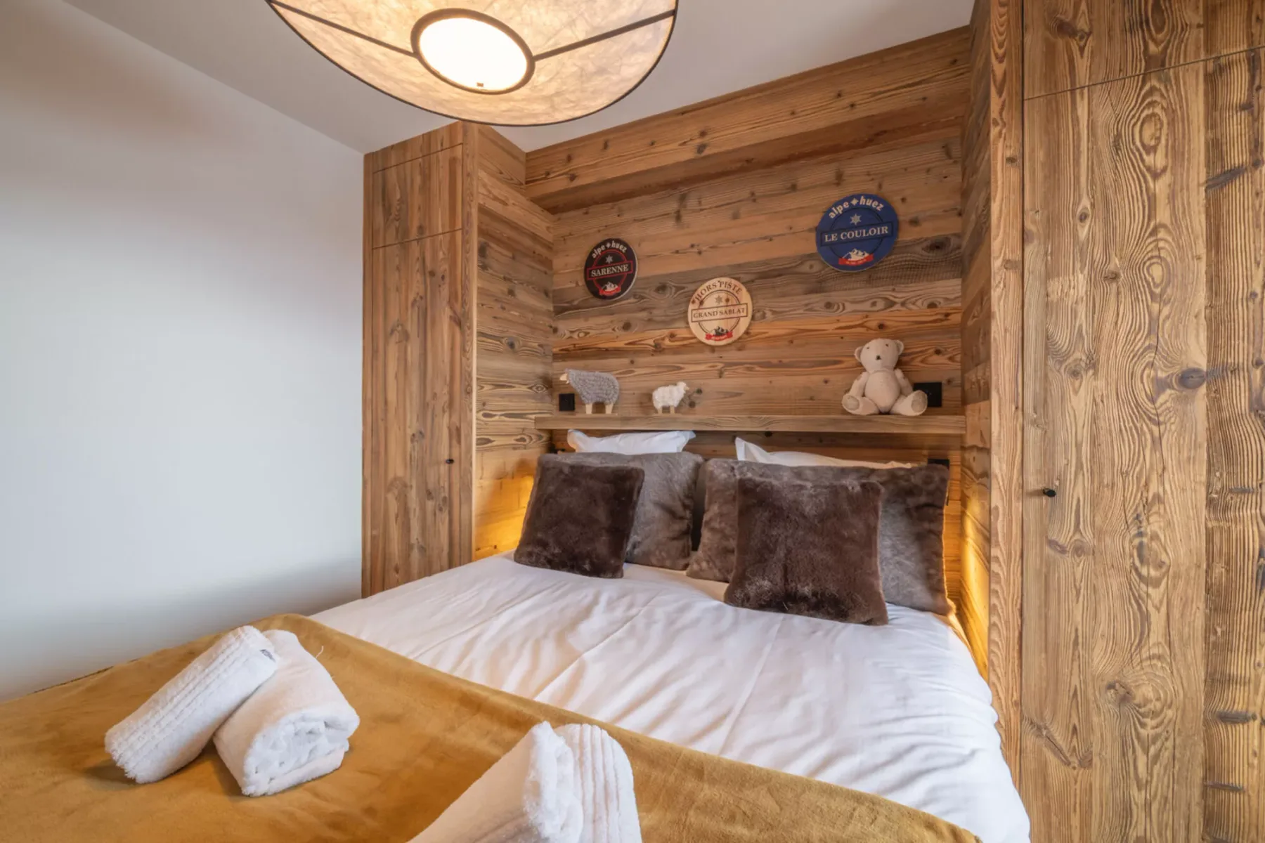 A bedroom with a bed beneath a wood-paneled wall and small shelf.