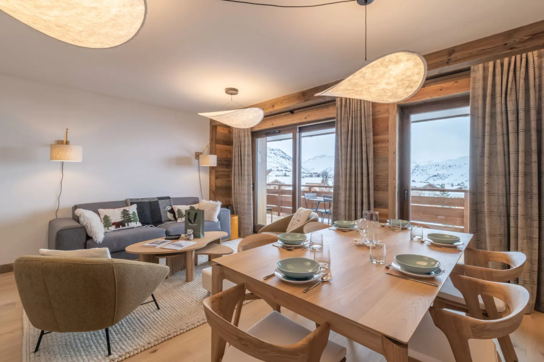 A dining and living area with a wooden table set beside large windows.