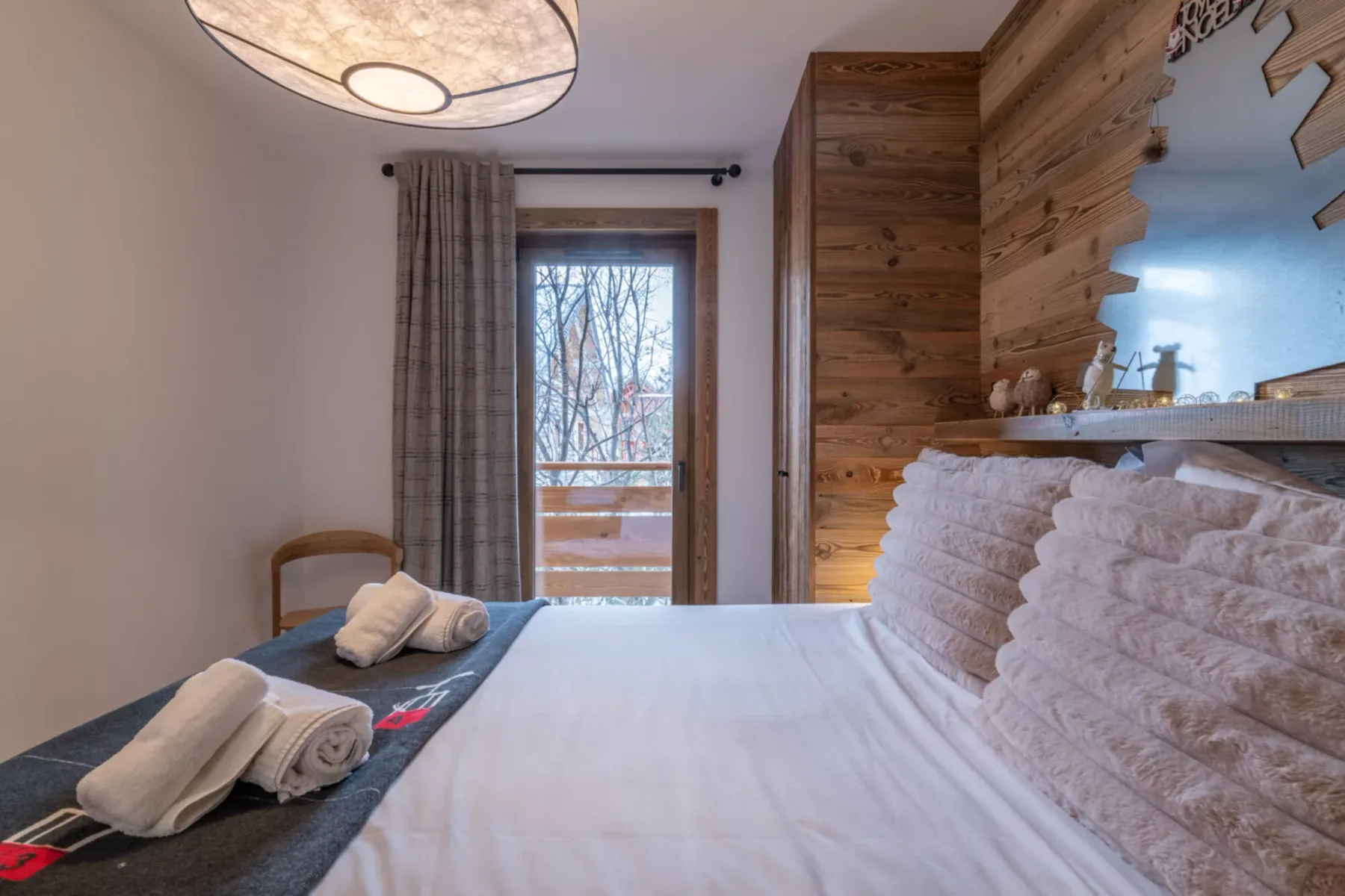A bedroom with a neatly made bed, folded towels, and a window.