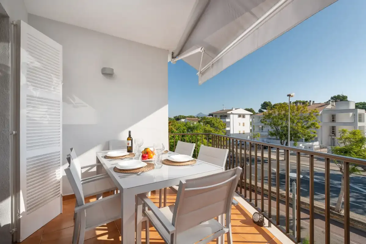 Comedor en un balcón con mesa y asientos, con edificios cercanos a la vista.