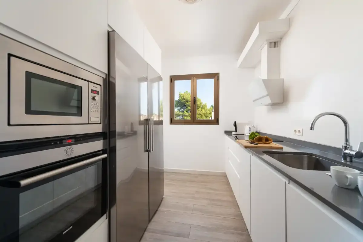 Una cocina luminosa con armarios blancos, encimeras oscuras y una ventana.