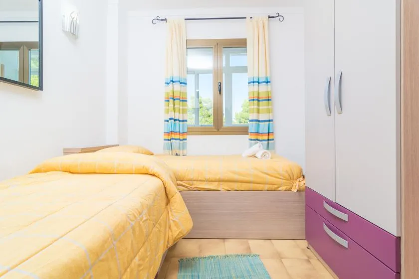 Un dormitorio con ropa de cama amarilla, una ventana y cortinas a rayas.
