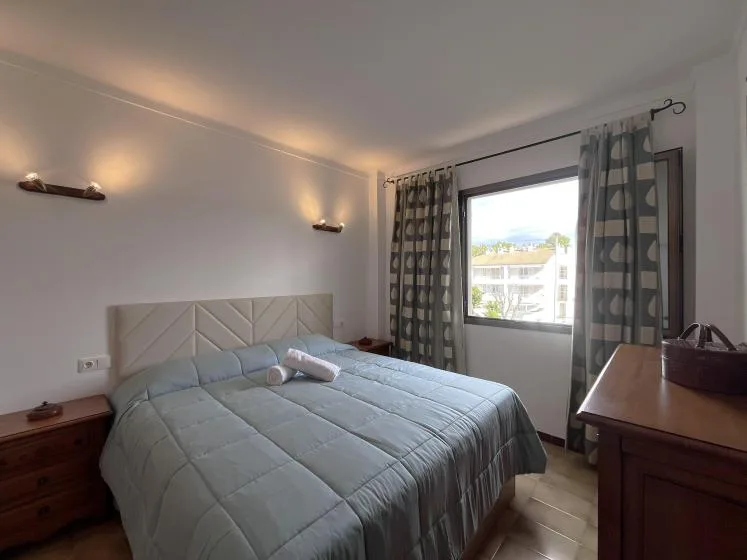 Un dormitorio con una cama, muebles de noche y una ventana con cortinas.