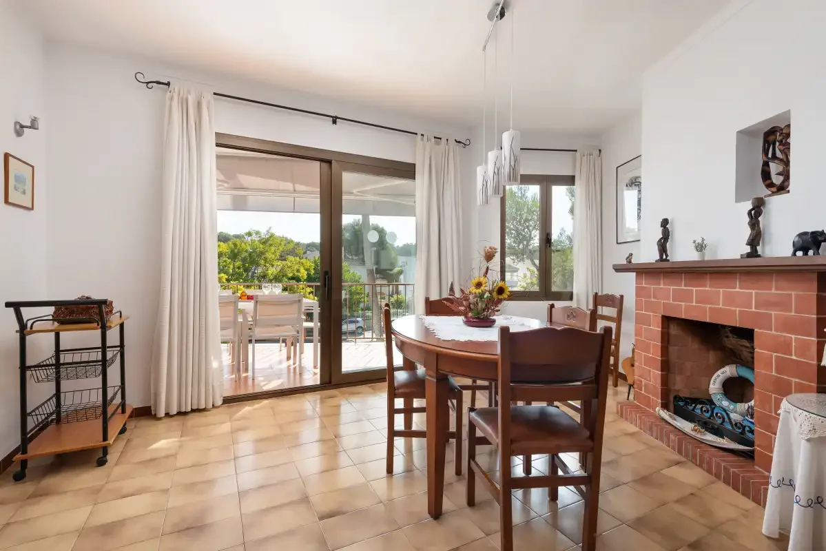 Comedor con una mesa de madera junto a grandes puertas de vidrio y una chimenea de ladrillo.