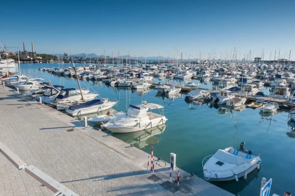Un puerto deportivo lleno de embarcaciones, con un muelle pavimentado junto al agua.