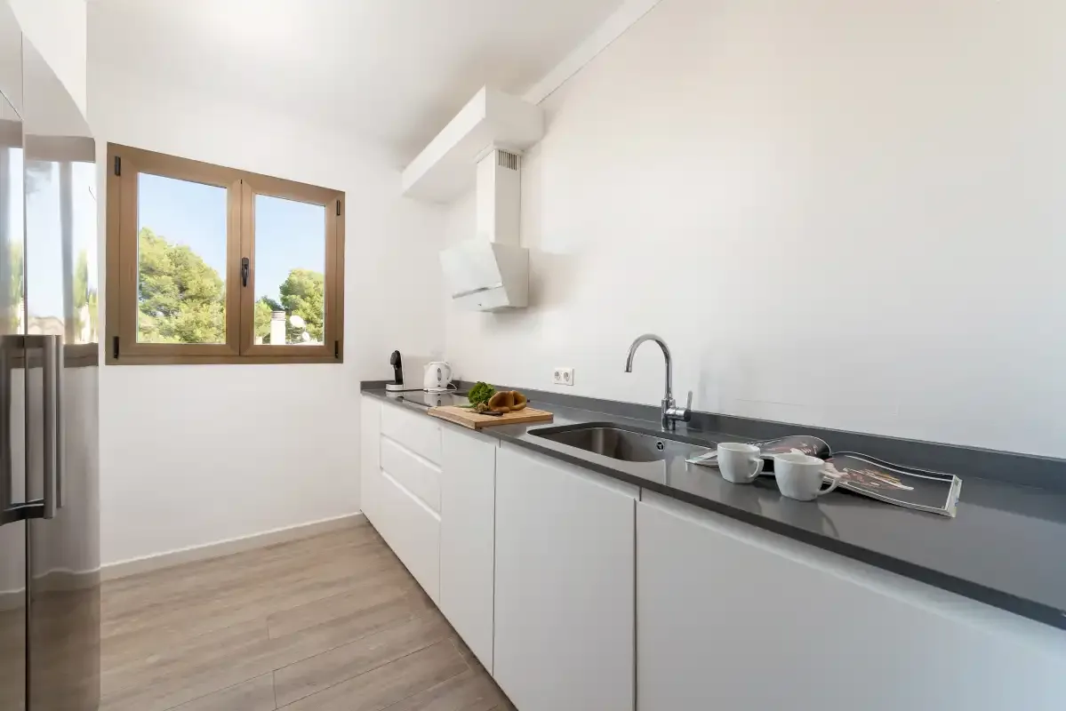 Una cocina luminosa con armarios blancos y una encimera larga.