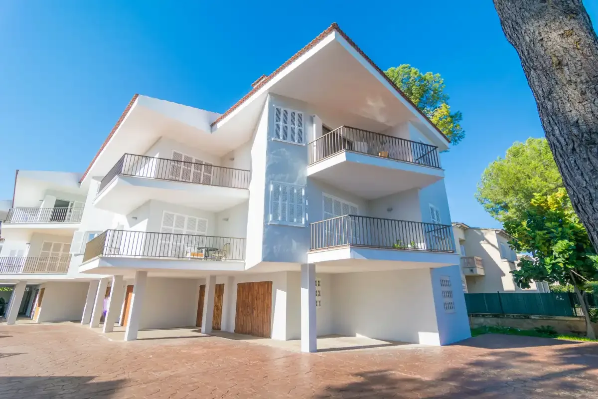 Un edificio de apartamentos blanco y moderno, con balcones y una entrada pavimentada.