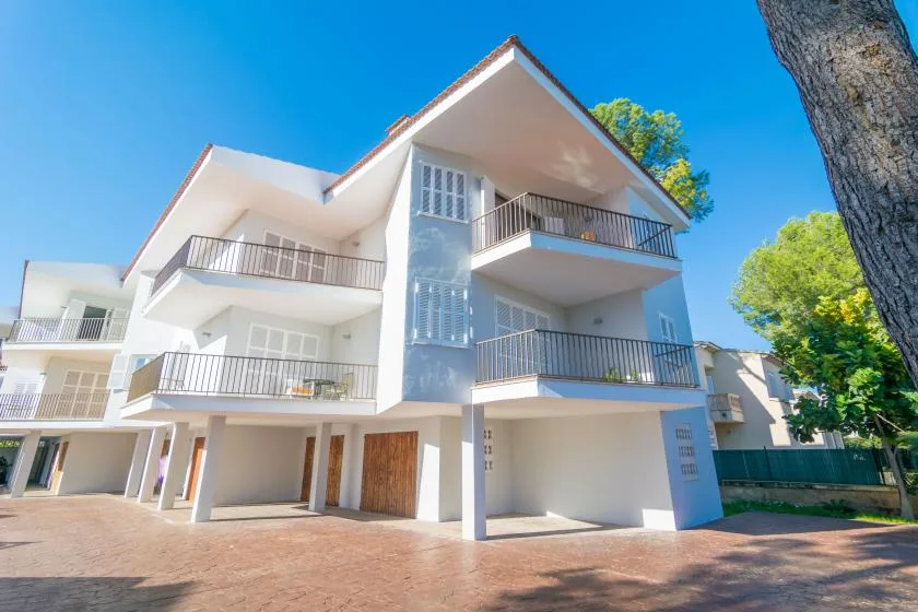Un edificio moderno de varios niveles con balcones se alza junto a un patio pavimentado.