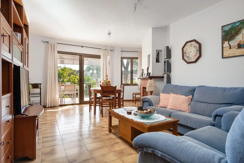 Una sala de estar y comedor con asientos azules y una mesa de madera junto a grandes ventanas.