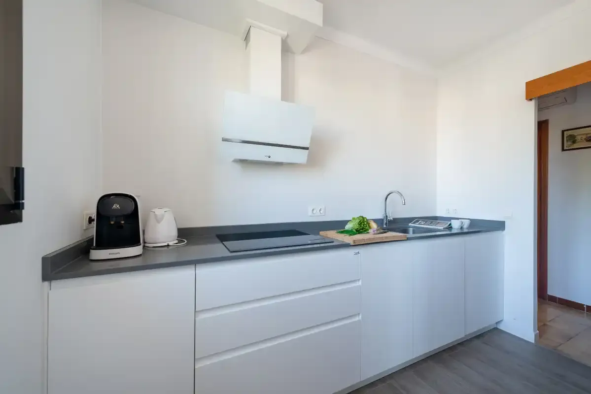 Una cocina moderna y luminosa con armarios blancos, una placa de cocina y un fregadero.