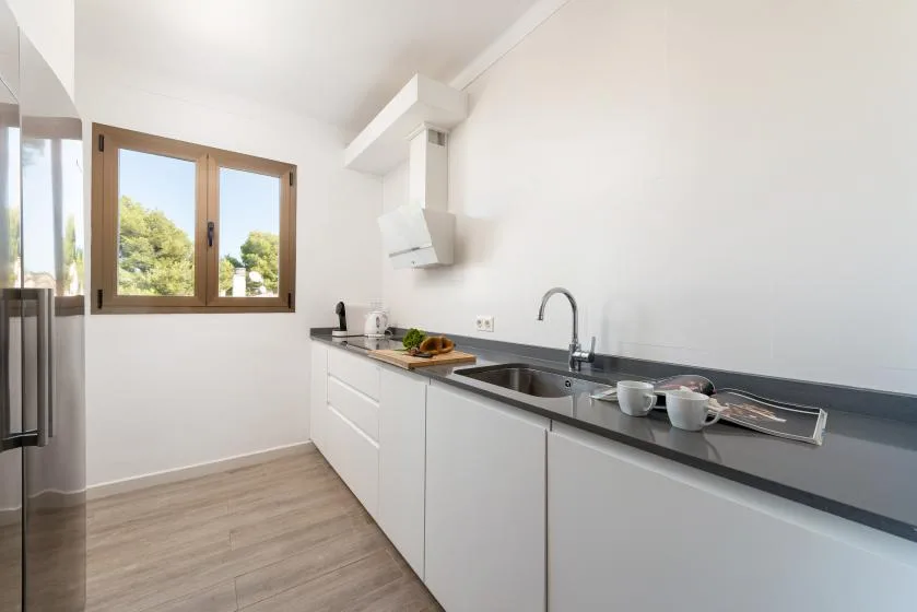 Una cocina luminosa con gabinetes blancos, una encimera oscura y una ventana.