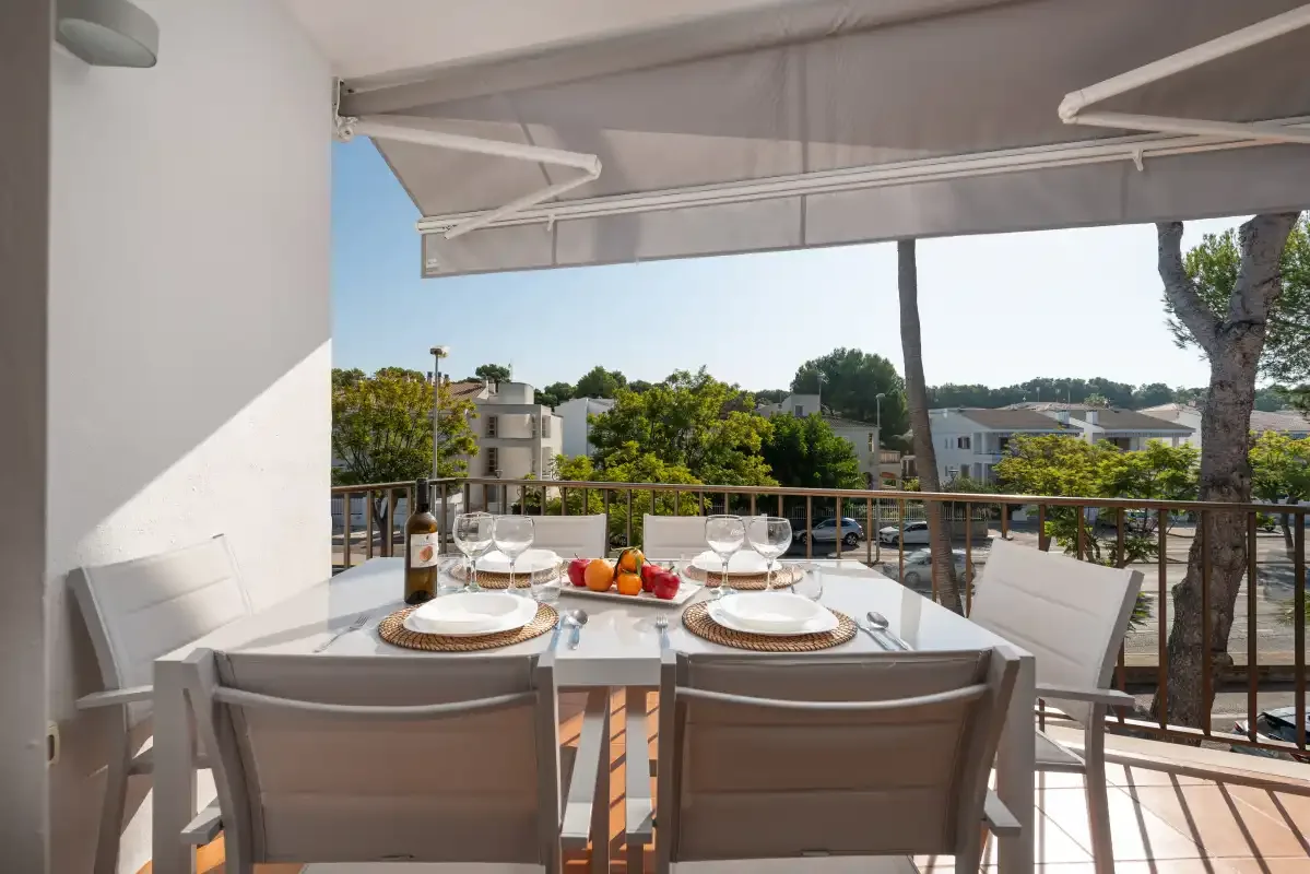 Una mesa de comedor al aire libre está preparada bajo un toldo en un balcón.