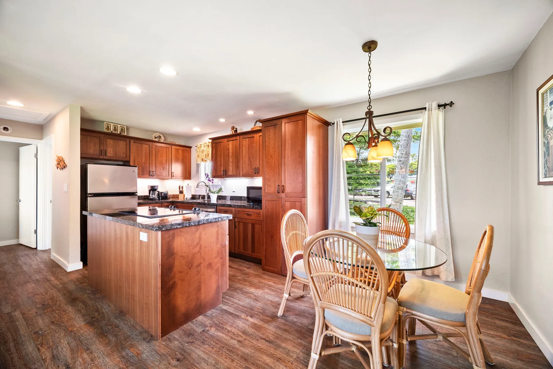 Cocina y comedor con gabinetes de madera, una isla y una mesa de comedor de vidrio.