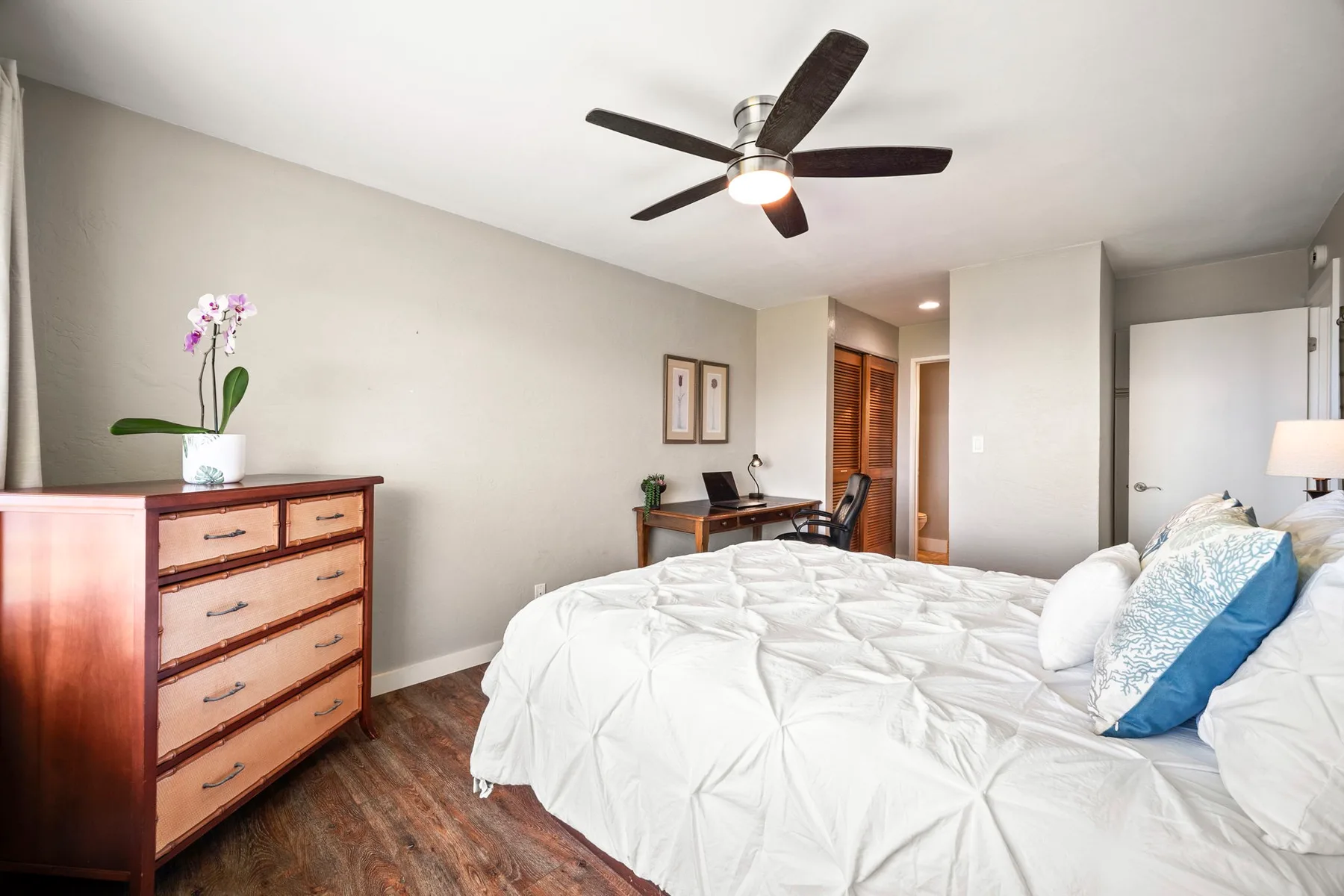 Un dormitorio con una cama, una cómoda de madera y un ventilador de techo.