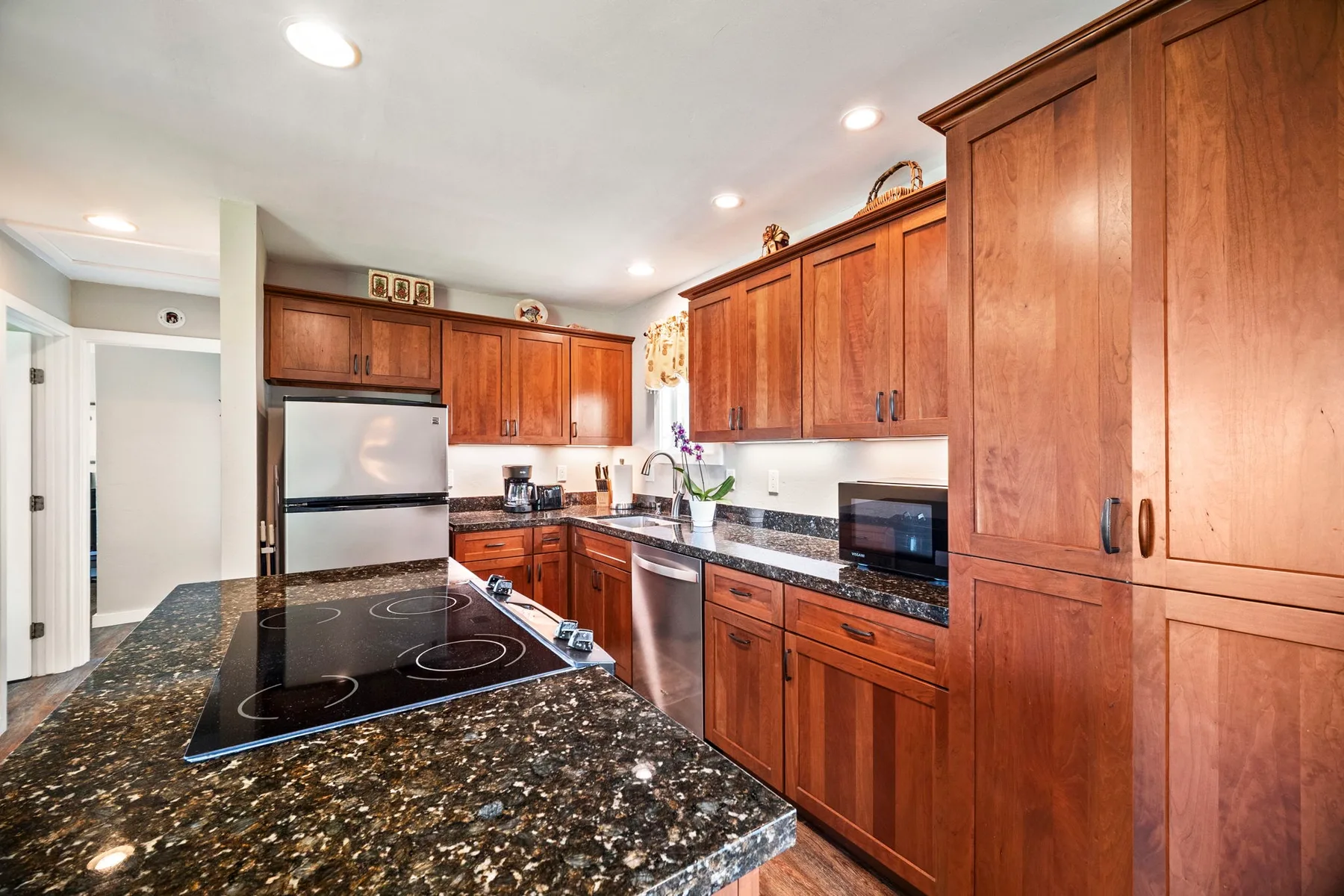 Una cocina con gabinetes de madera rojiza, encimeras oscuras y una placa de cocina.