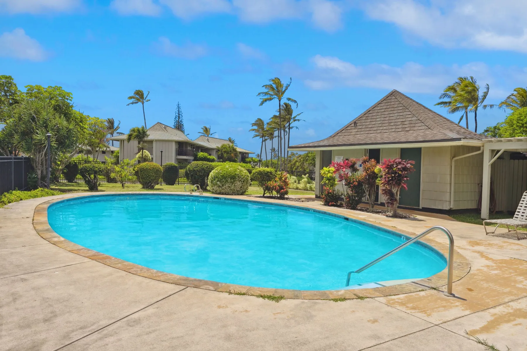 Una piscina exterior curva está junto a un pabellón bajo y vegetación tropical.