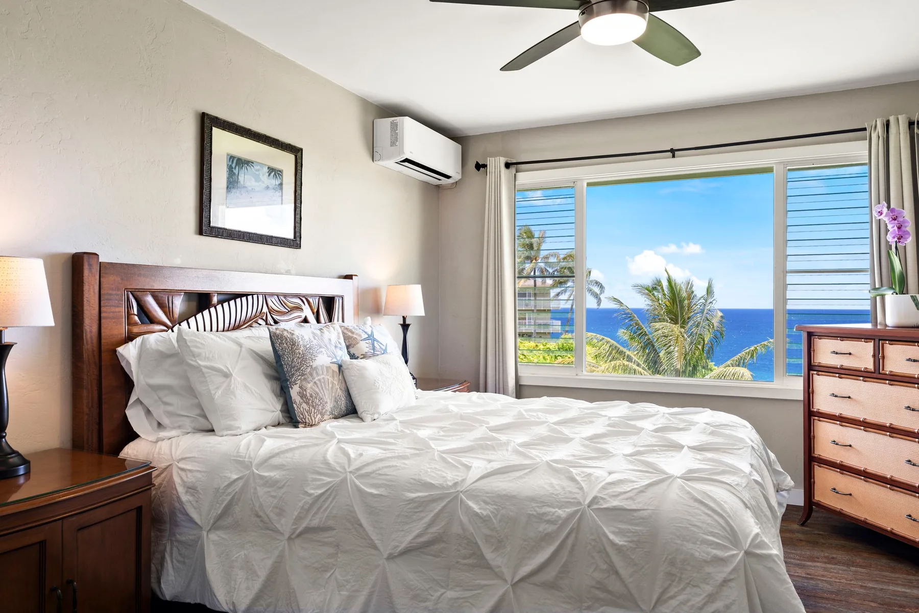 Un dormitorio con una cama bien tendida frente a una ventana grande con vista al mar.