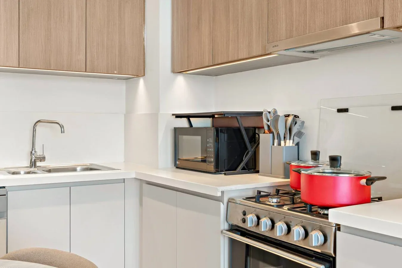 A modern kitchen with wood cabinets, a countertop, and a red pot on the stove.