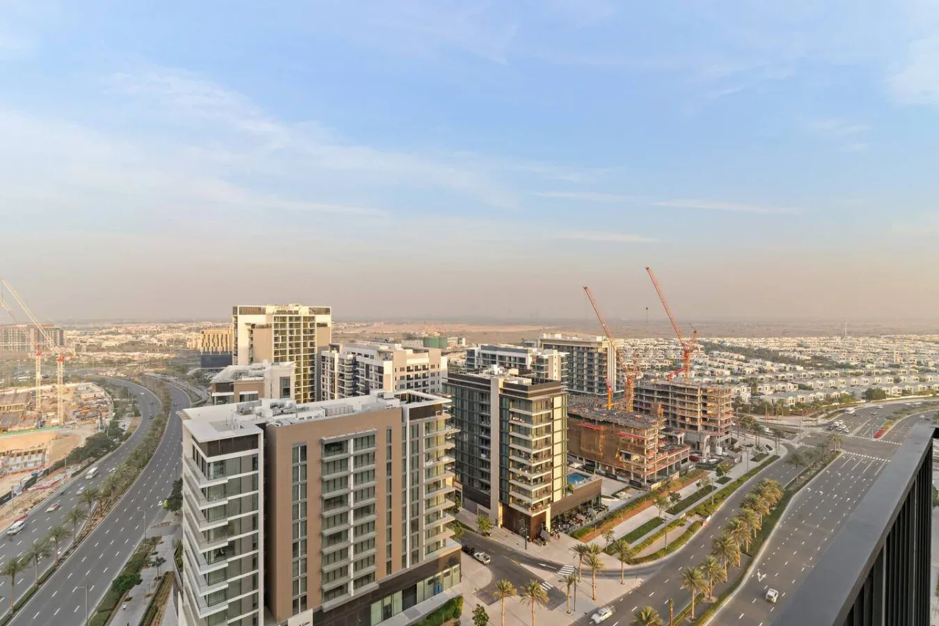 Aerial view of modern buildings, construction cranes, and roads beneath a hazy sky.