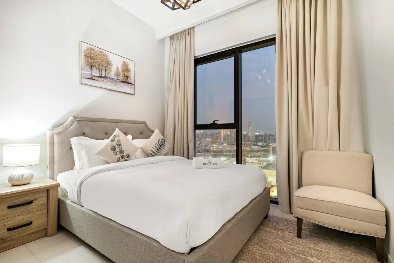 A bedroom with a neatly made bed beside a large curtained window.