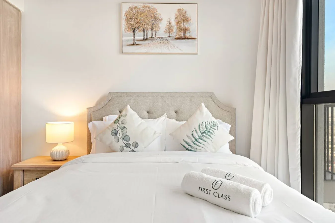 A bedroom with a neatly made bed and a framed landscape above the headboard.