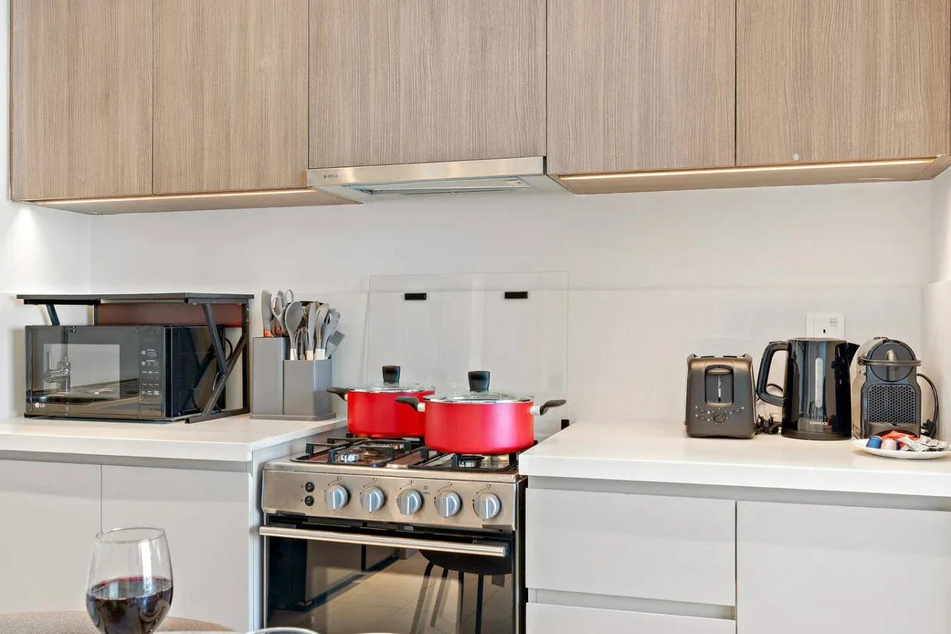 A bright kitchen with a stove, red pots, and countertop appliances.