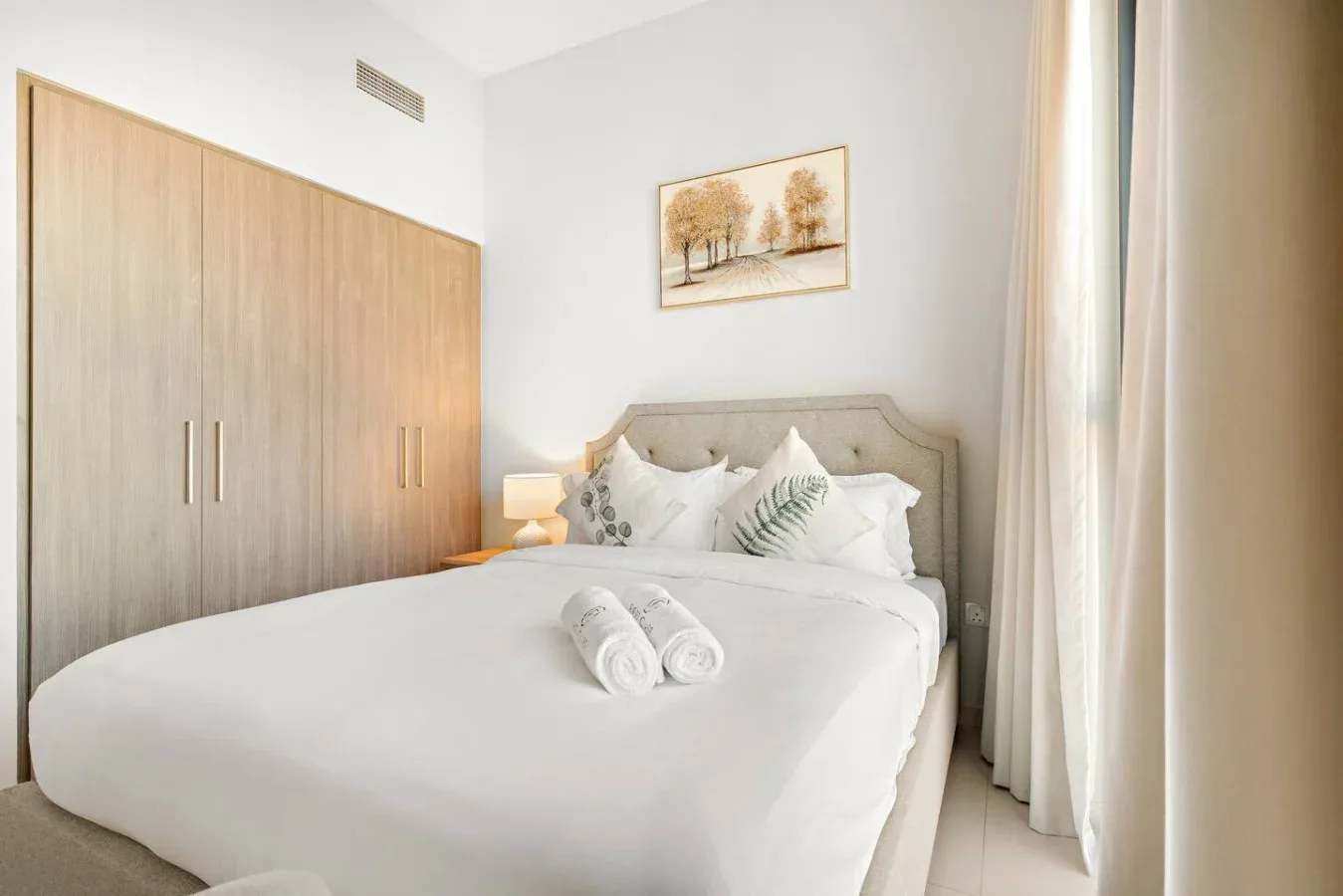 A bright bedroom with a neatly made bed, bedside lamp, and built-in wardrobe.