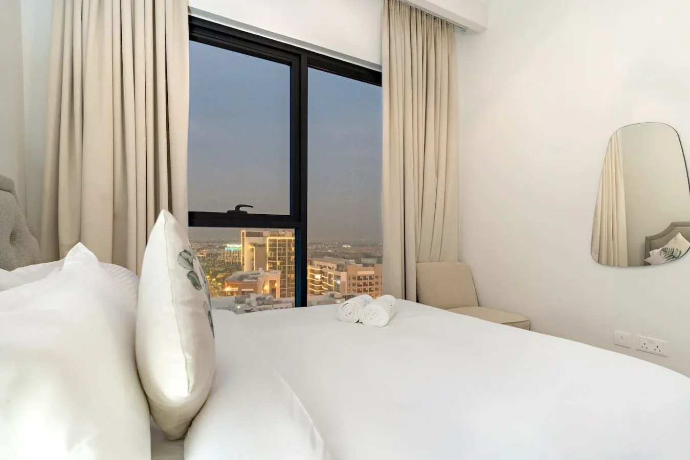 A bedroom with a neatly made bed beside a large curtained window.