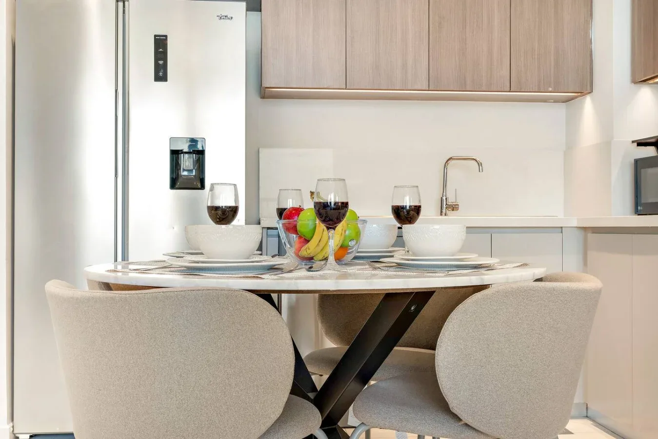 A dining area with a round table set with dishes and glasses beside the kitchen.