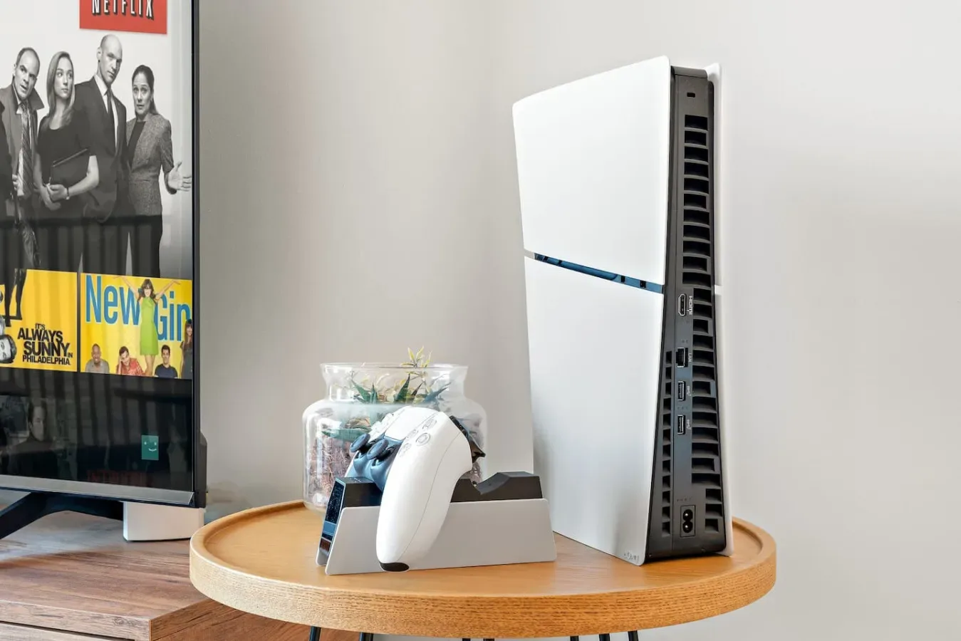 Una mesa redonda de madera muestra un ventilador de torre blanco y pequeños objetos decorativos junto a un televisor.