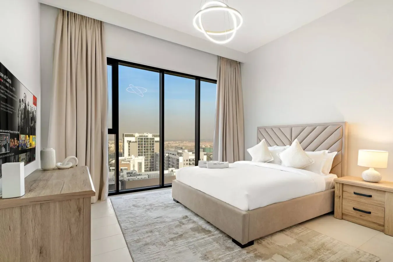 Un dormitorio luminoso con una cama bien hecha junto a grandes ventanas con vistas a la ciudad.