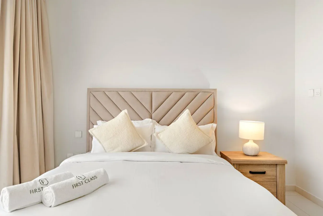 A bedroom with a neatly made bed and a wooden bedside table.
