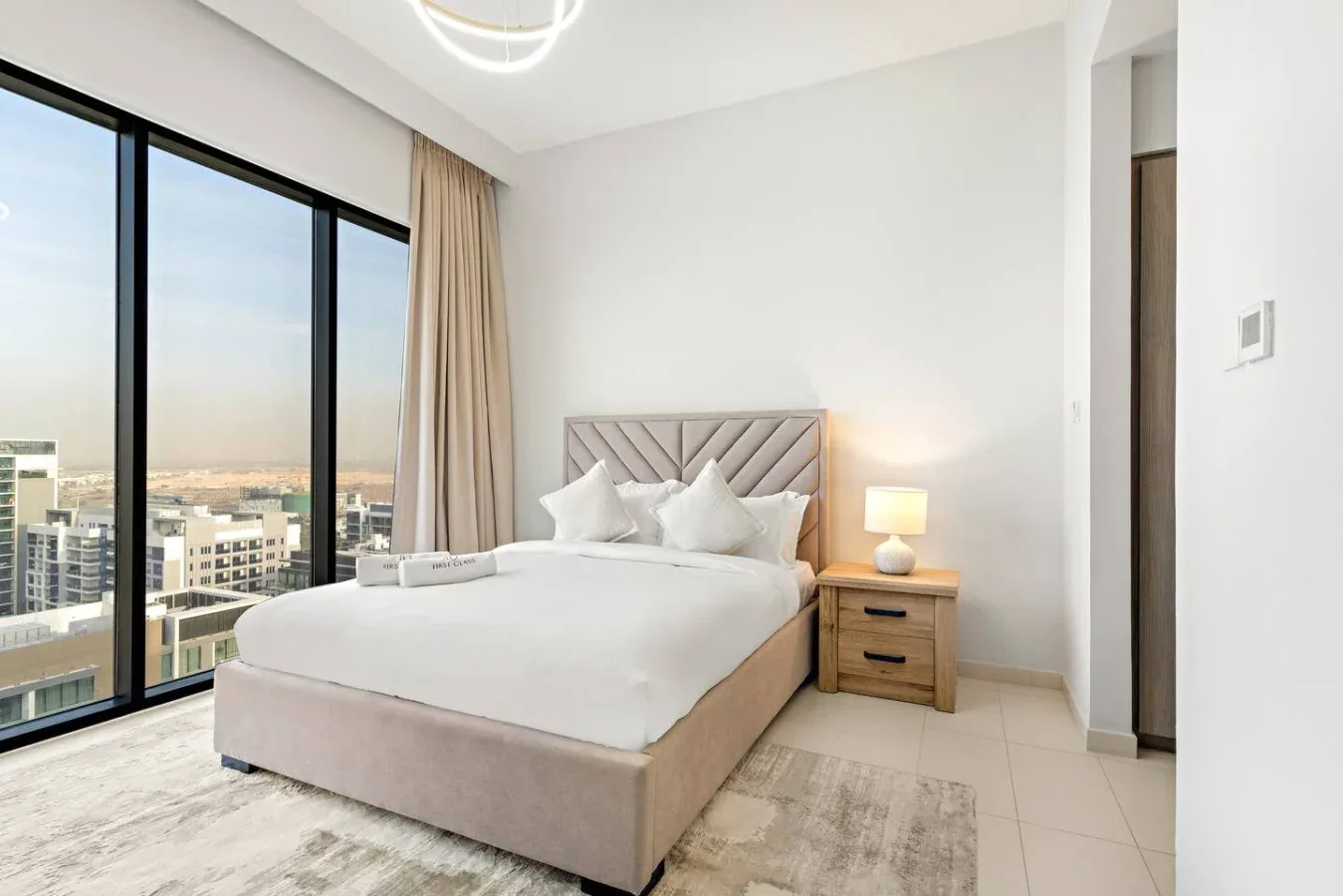 A bright bedroom with a large bed beside floor-to-ceiling windows.
