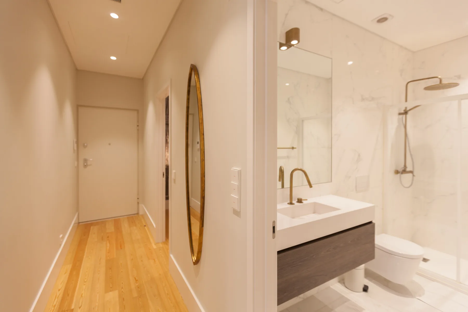 Un pasillo luminoso conduce a un baño con lavabo, inodoro y ducha.
