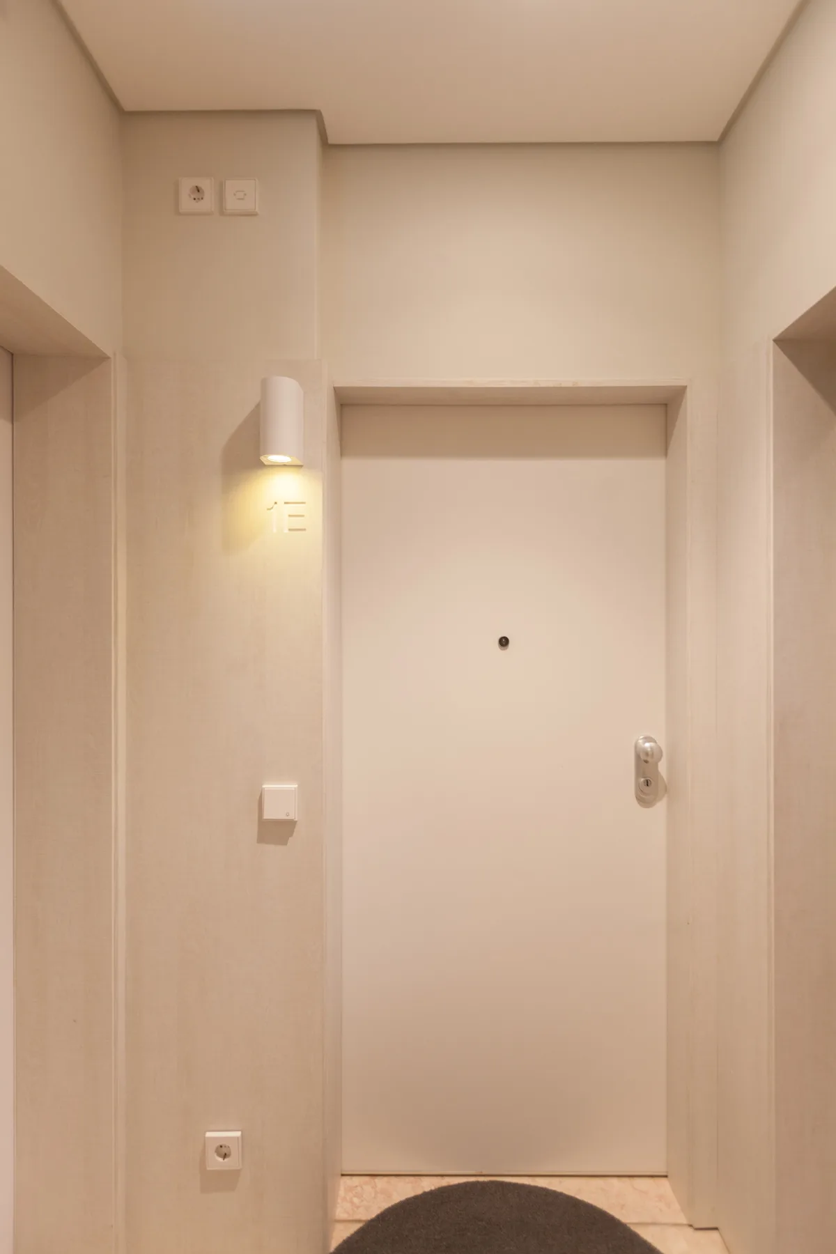 A plain interior doorway with a wall light and a small round peephole.