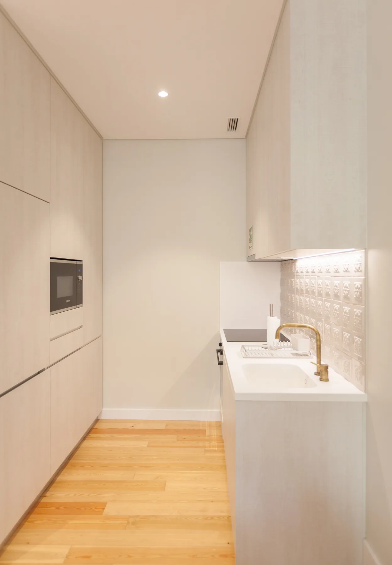 A narrow kitchen with light cabinetry, a countertop, and a sink.