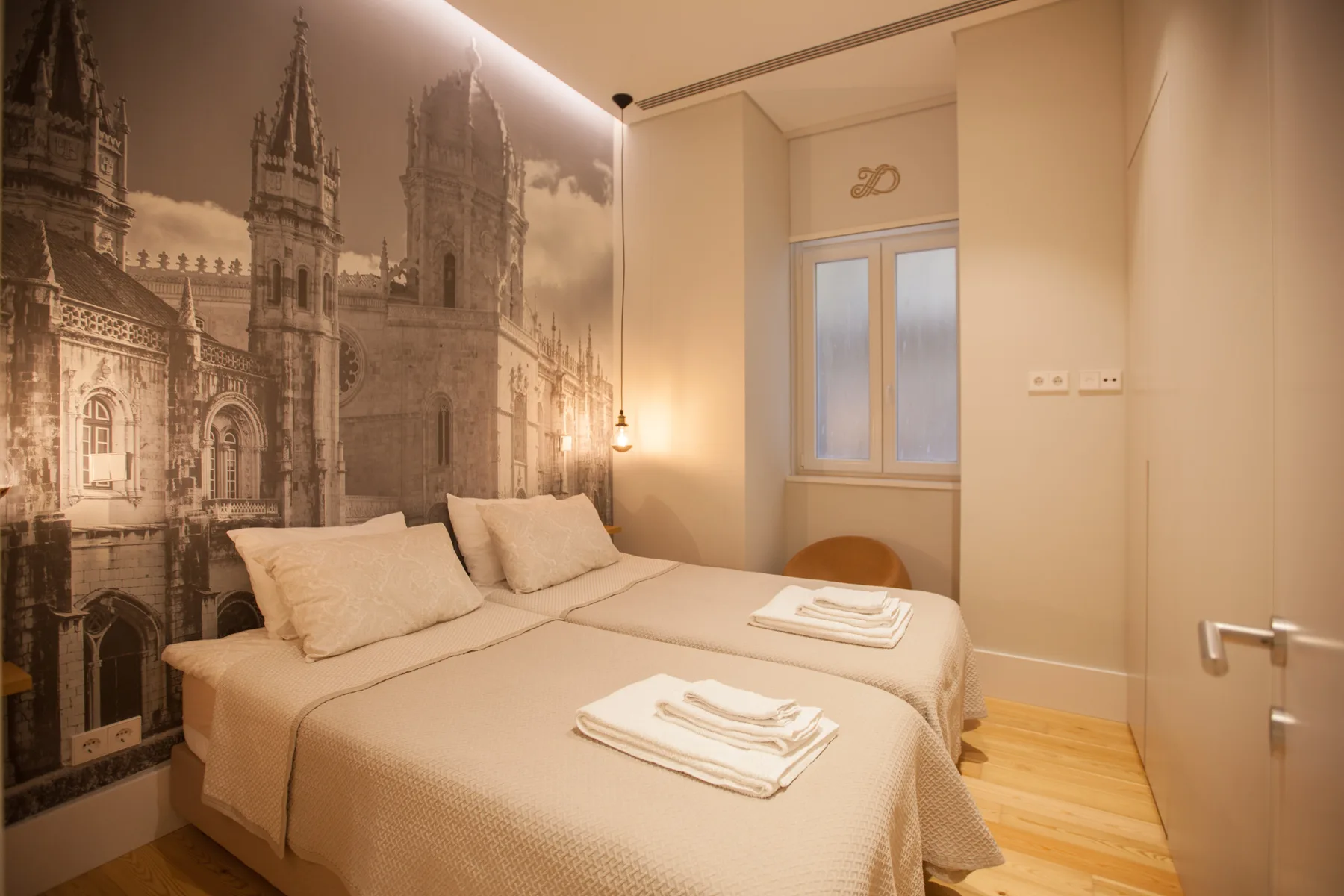 A bedroom with two beds, folded towels, and a sepia city mural.