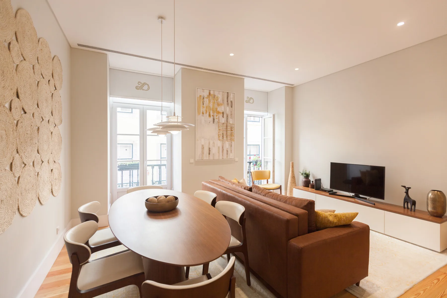 A bright living and dining area with a brown sofa and oval dining table.