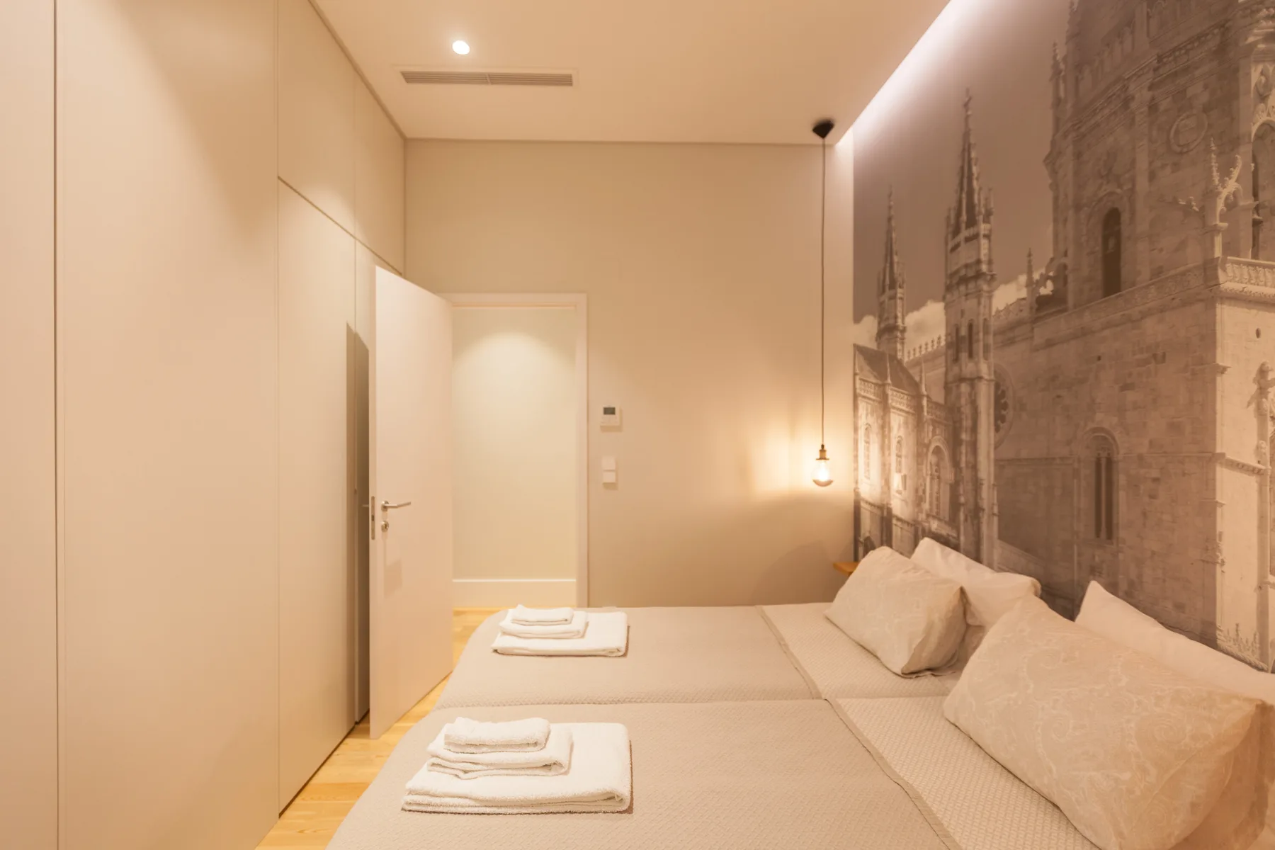 A bedroom with two beds, folded towels, and a large architectural wall mural.