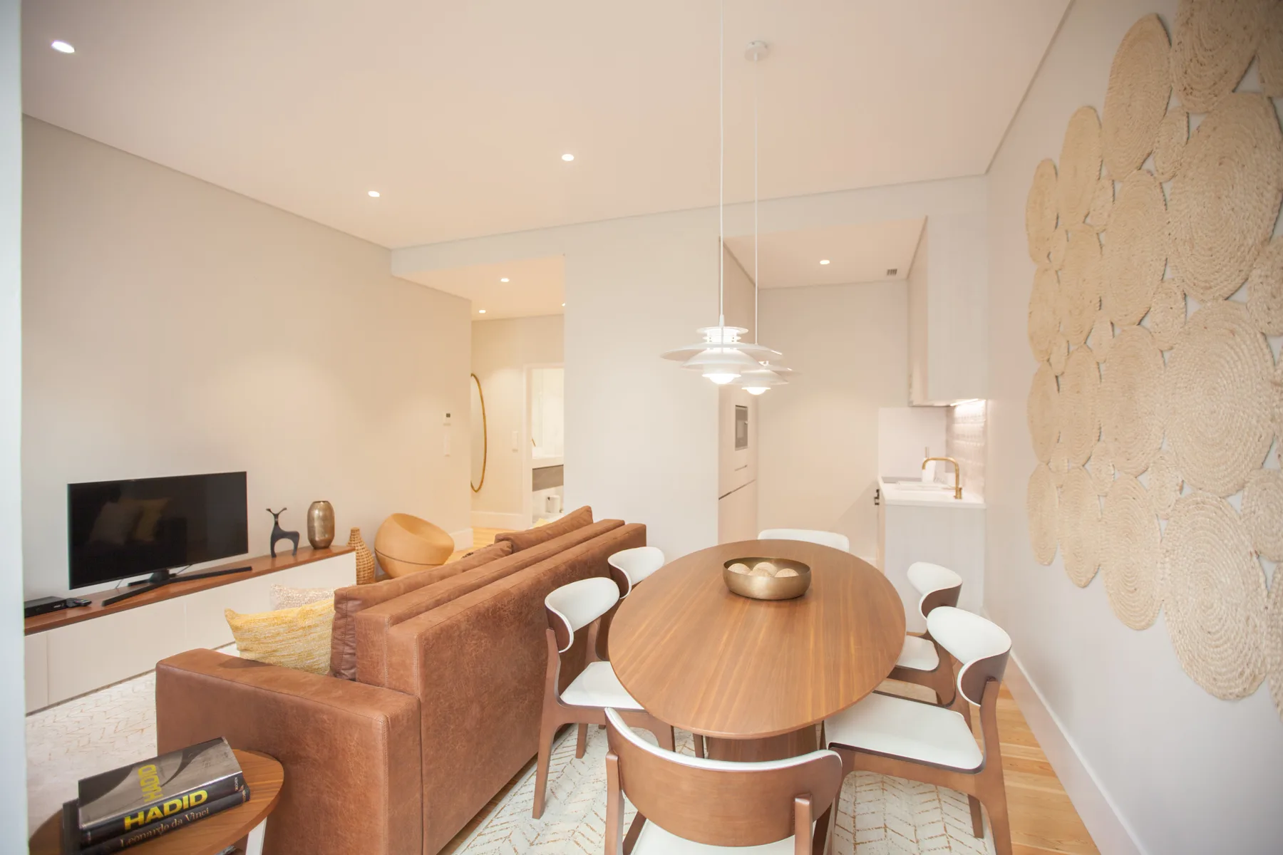 A bright living and dining area with a television, seating, and an oval dining table.
