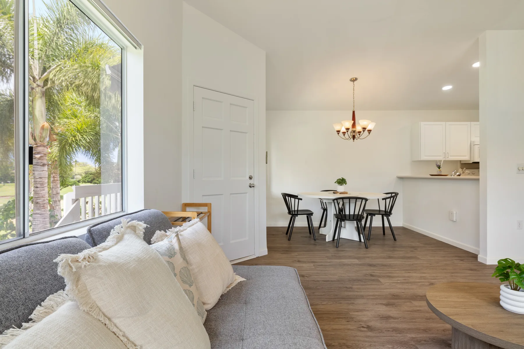 Living room with seating beside a window overlooking greenery, with a dining area beyond.
