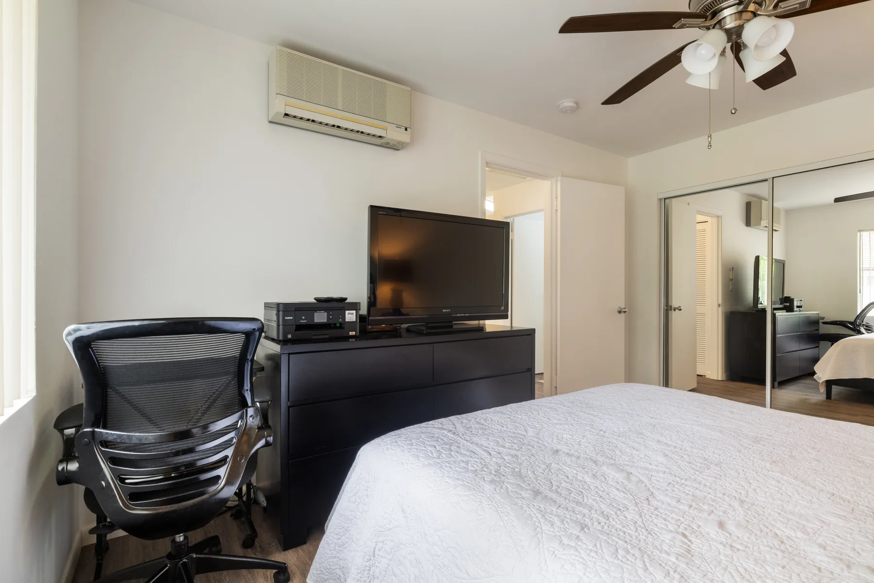 A bedroom with a bed, desk chair, television, and mirrored closet doors.