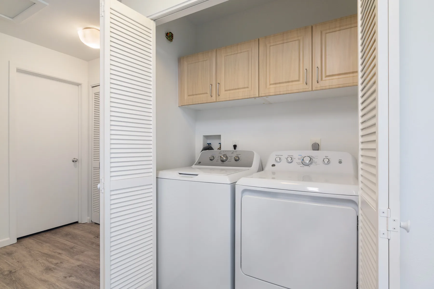 A laundry area with a washer and dryer beneath wooden cabinets.