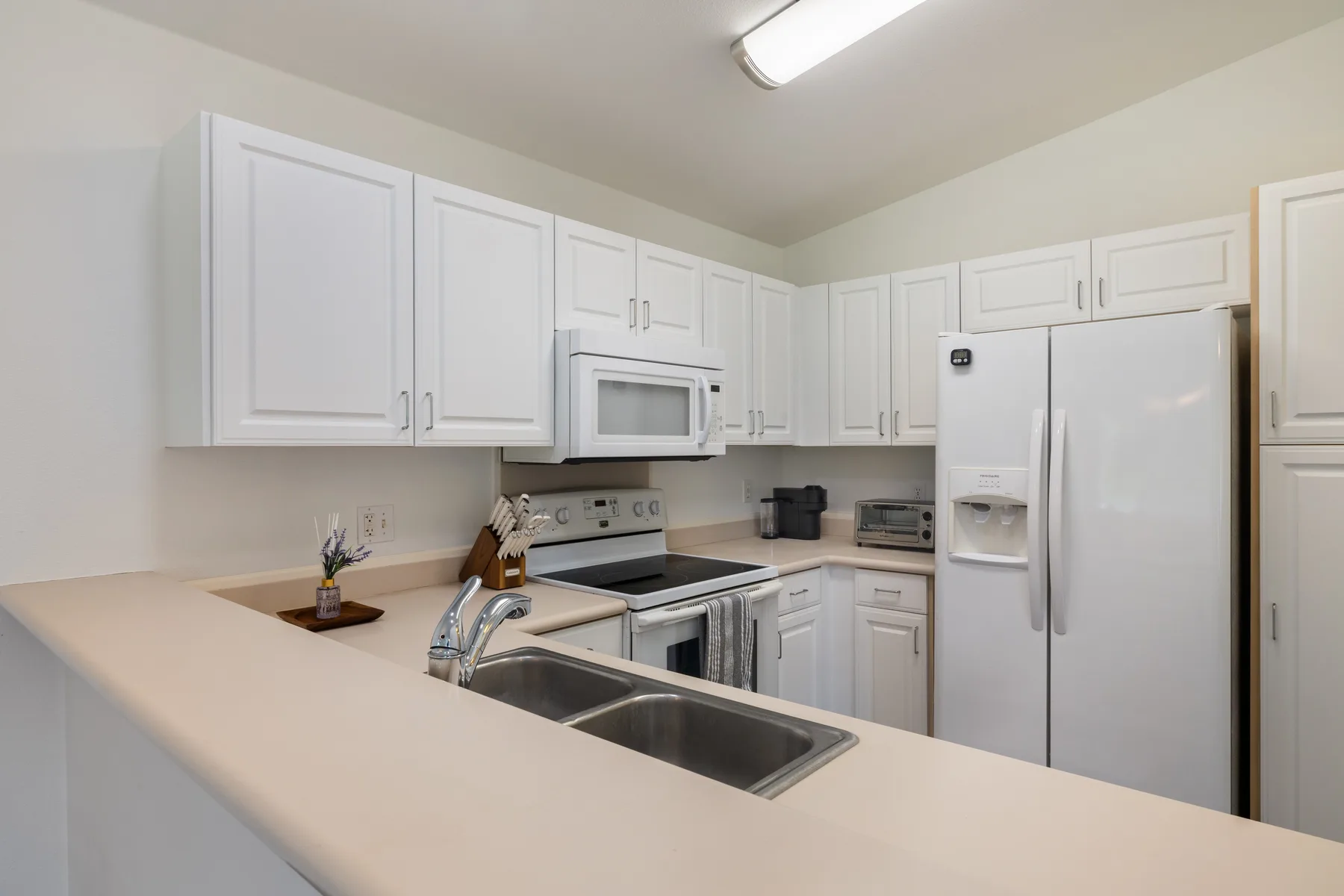 A bright kitchen with white cabinets, a refrigerator, and a double sink.