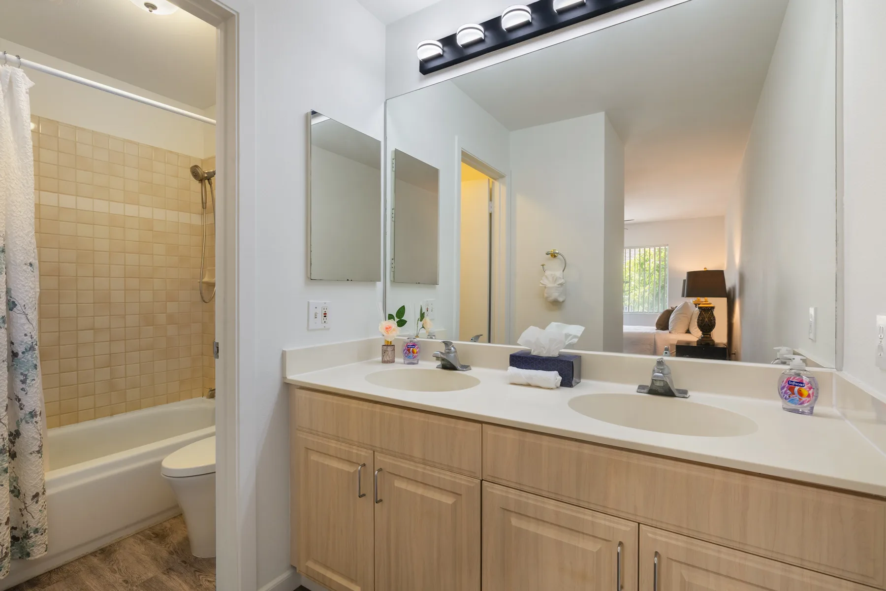 A bathroom vanity with two sinks and a large mirror beside a bathtub.