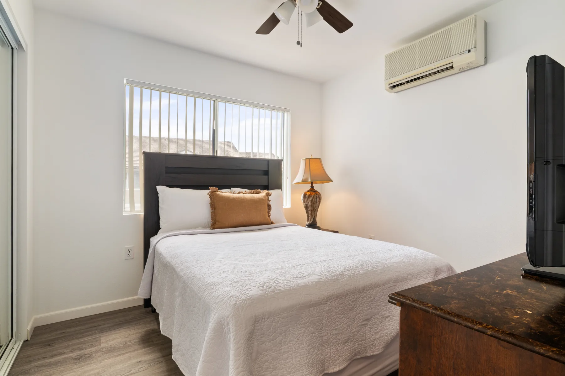 A bedroom with a neatly made bed beneath a window with vertical blinds.