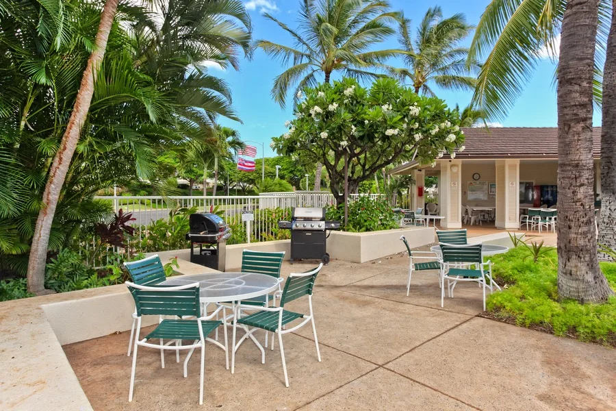 A tropical outdoor patio has green seating, a grill, and palm trees.