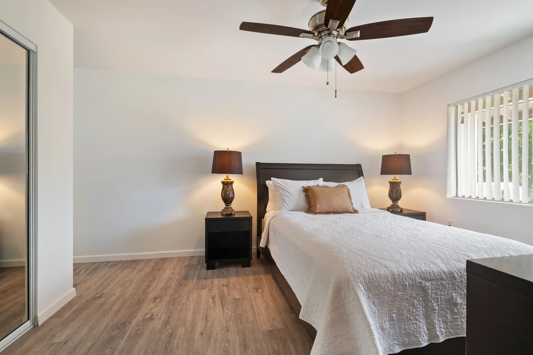 A bedroom with a bed, matching bedside tables, and a ceiling fan.