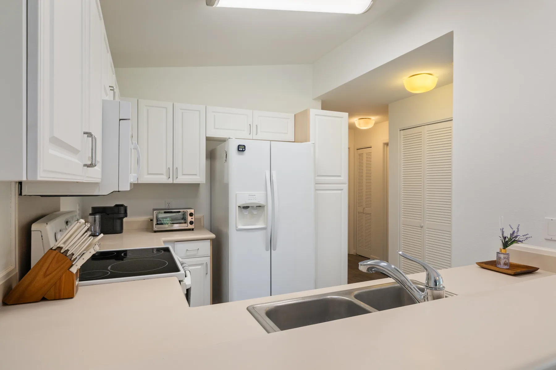 A bright kitchen with white cabinets, a refrigerator, and a double-basin sink.